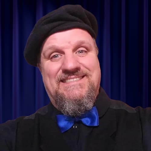 A friendly headshot of Will Walker, a man with a goatee, smiling warmly at the camera. He is wearing a black beret, a dark jacket, and a vibrant blue bow tie, posed in front of a royal blue curtain.